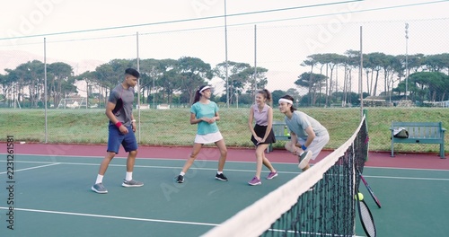 Diverse friends wearing athletic clothing, playing near net on hardcourt with rackets, tennis ball