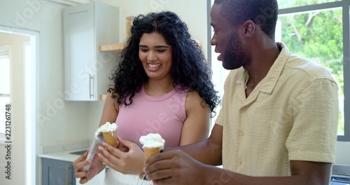 Fotografie Diverse couple sharing ice cream cones while standing at kitchen counter, woman