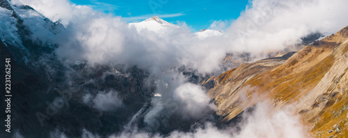 Obraz na plátně Aerial view of the Grossglockner massif and Pasterze Glacier in Austria, surrounded by dramatic clouds, rugged alpine peaks and sunlit golden mountain slopes in the Hohe Tauern