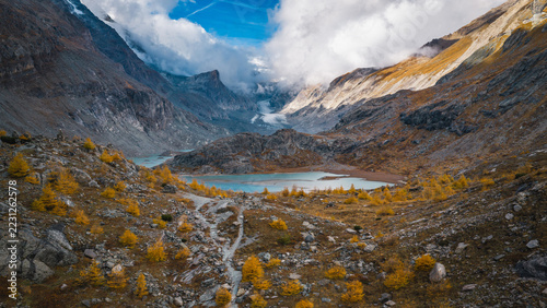 Obraz na plátně Panoramic alpine landscape near Grossglockner in Austria, featuring the Pasterze Glacier, a turquoise glacial lake, rugged rocky slopes, golden autumn vegetation and dramatic clouds