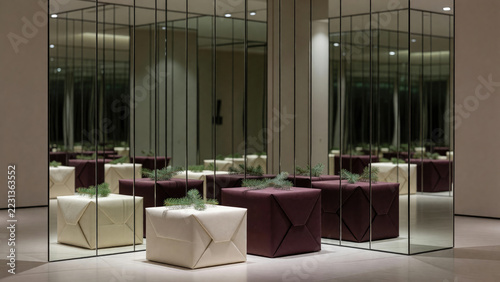 Geometric upholstered ottomans with evergreen branches in mirrored modern interior. Contemporary furniture and interior design. Reflective architecture and spatial illusion.