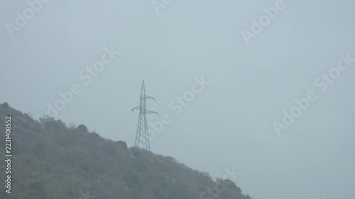 Transmission tower on rocky hillside under overcast sky
