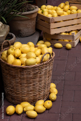Fresh yellow lemons piled in rustic woven basket and wooden crates at an outdoor market, creating a vibrant display of Mediterranean produce.
