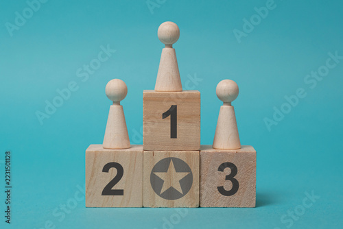 Wooden Figures on Winners Podium with Numbered Blocks on Turquoise Background