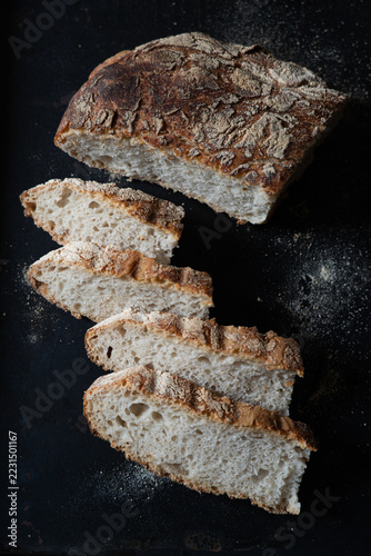 Rustic Bread Loaf and Slices on Dark Background with Scattered Flour