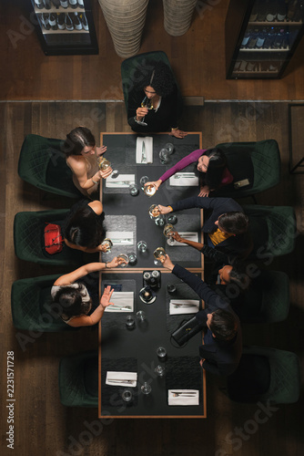 A group of friends and colleagues raise wine glasses around joined tables during a dinner year end party at a restaurant in the evening.