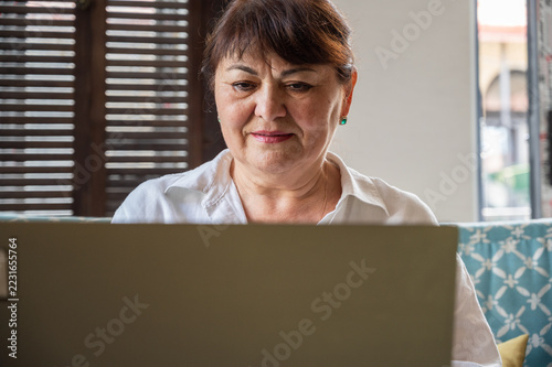 Concentrated senior female teacher or businesswoman using laptop while working at home