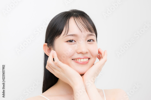 白背景で顎や頬に両手を添える10代～20代のような若い女性の美容やビューティーの笑顔　ニキビや思春期の肌の嬉しいハッピーなティーンのイメージ　カメラ目線