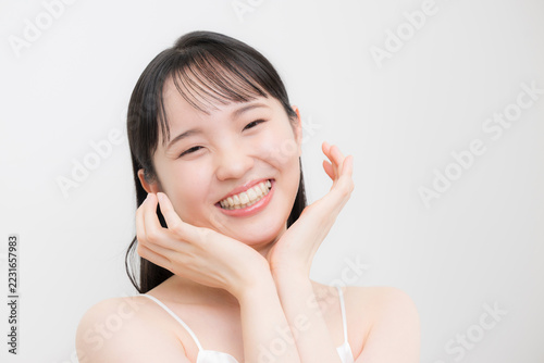 白背景で顎や頬に両手を添える10代～20代のような若い女性の美容やビューティーの笑顔　ニキビや思春期の肌の嬉しいハッピーなティーンのイメージ　カメラ目線