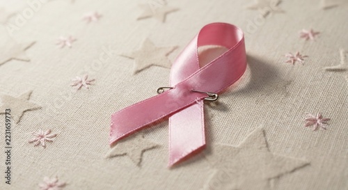 Pink awareness ribbon on textured fabric surface with stars and embroidery