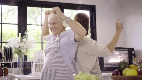 Happy senior couple wearing aprons dancing together in modern kitchen