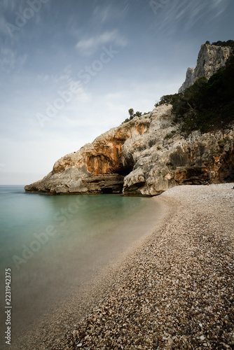 Pebble beach with rocky cliffs at Cala Sisine in Sardinia, Italy
