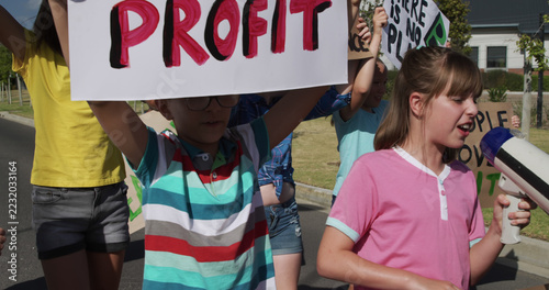 Happy diverse elementary schoolchildren with ecology placards protesting in sunny street