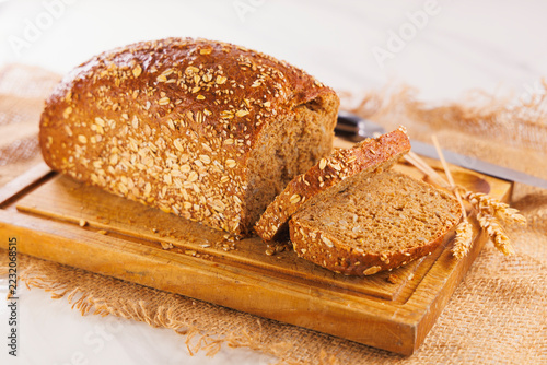 Obraz na plátně Fresh whole grain bread sliced on wooden cutting board with wheat ears and knife