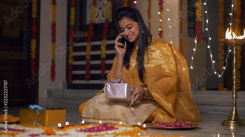Beautiful Indian girl talking on phone with Diwali gift in her lap. 