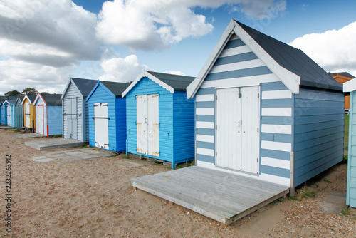 Colorful beach huts line a sandy coast under a cloudy sky