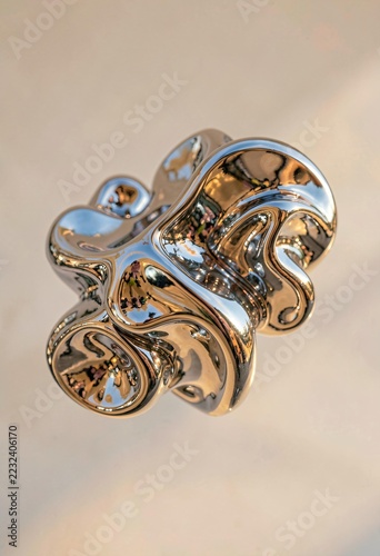Abstract liquid metal sculpture with shiny chrome reflective surface against neutral background indoors