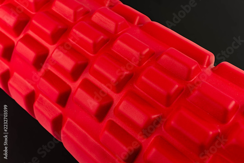 Vibrant red massage foam roller on black background.