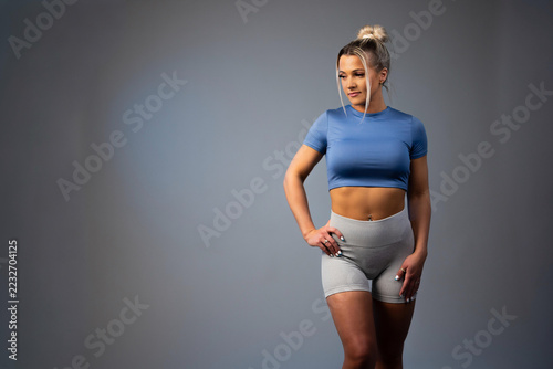 Fit young woman in blue crop top and gray leggings standing confidently in studio