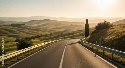 Paved road curves through rolling hills under a hazy sky, with a lone tree