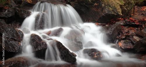Panorama of a beautiful autumn waterfall flowing over rocks in a colorful forest, peaceful nature scene, long exposure