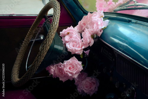 Pink roses arranged inside a vintage convertible car. Floral decoration for a wedding getaway. Romance, celebration and elegant automotive style. Classic car interior with flower bouquet.