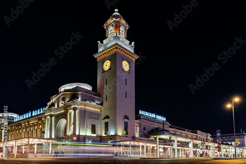 Illuminated Kievsky Railway Station clock tower above Moscow traffic at night. Historic railway terminal and urban transport hub. City travel and commuter transit. Long exposure light trails
