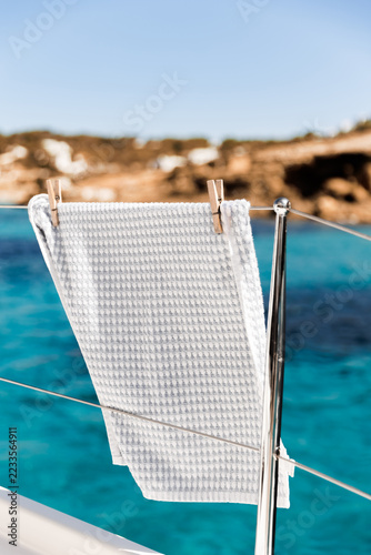 A white towel drying on a sailboat railing under the summer sun with a beautiful turquoise sea in the background. Vertical stock photo