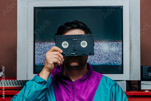 Man in retro 80s jacket holding VHS tape over face, TV static backgroun