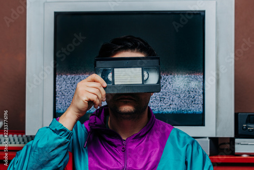Man in retro 80s jacket holding VHS tape over face, TV static backgroun