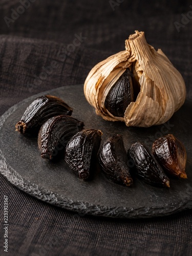 Black garlic cloves and a whole bulb arranged on a dark slate board