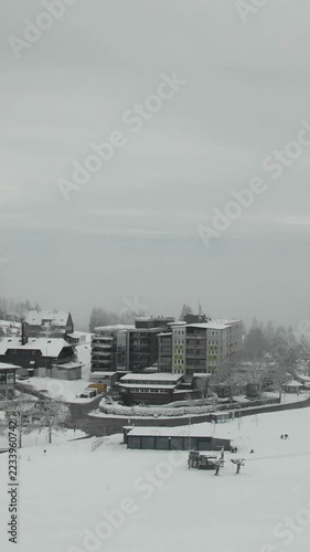 Vertical timelapse footage of a snowy alpine village gradually disappearing under an incoming white fog layer.