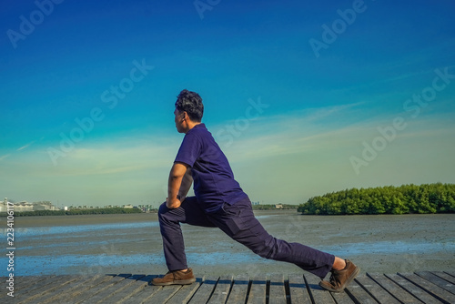 Fotografie Young man doing stretching exercises on a wooden dock at a mangrove forest in br