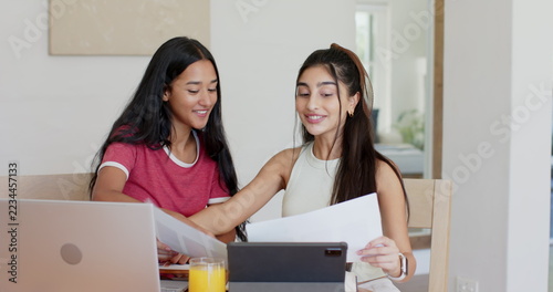 Diverse female friends reviewing papers with laptop, tablet and orange juice at dining table
