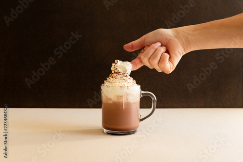 Chocolat chaud dans une tasse en verre avec le doigt d'une main qui trempe dans la crème chantilly