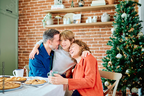Fotografie Family embracing and laughing together beside a decorated Christmas tree, sharin