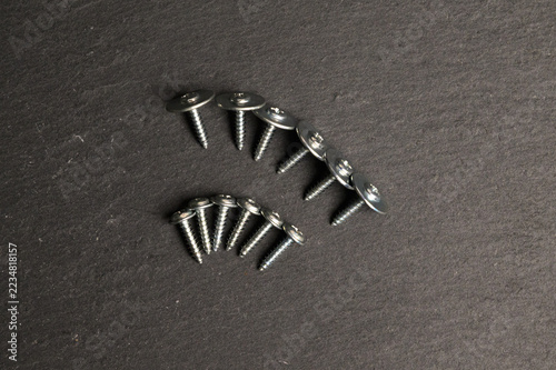 Top view of metal self-tapping screws arranged in curves on dark slate surface