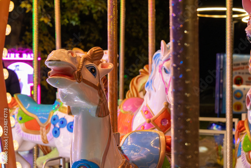 Carousel horses stand between metal poles at an amusement park at night
