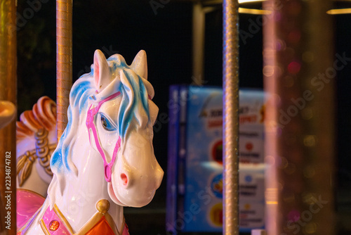 Painted carousel horse stands among the poles of a fairground ride at night