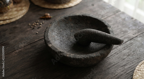 Traditional stone mortar and pestle resting on a wooden table with cooking spices in a rustic kitchen setting