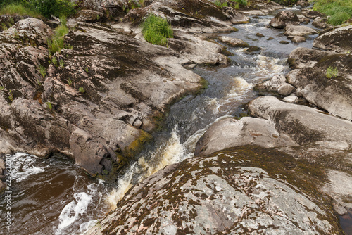 White water rapids rush through a channel carved in smooth eroded bedrock.