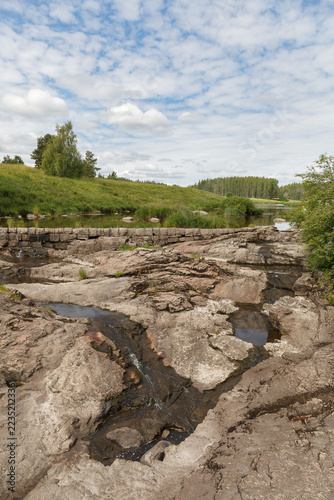 Shallow stream cuts through smooth gray bedrock beside a grassy riverbank.