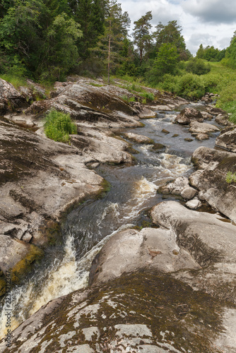 Foaming rapids cut through layered bedrock in a forested river valley.