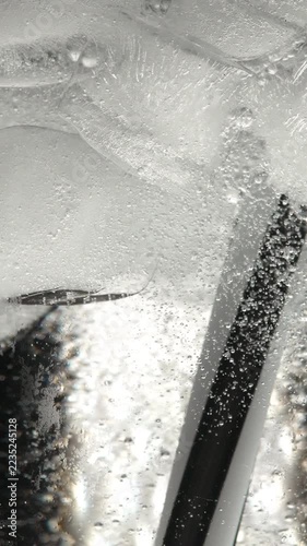 A close-up of a glass containing carbonated water, ice, and a straw, with gas bubbles rising to the surface.