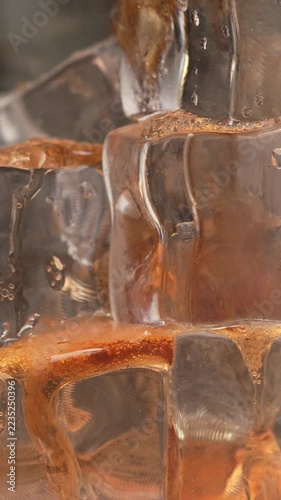 A close-up shot of ice cubes as a refreshing, sweet soda drink is slowly poured over them. Macro footage of a chilled, refreshing beverage, complete with bubbles and liquid.