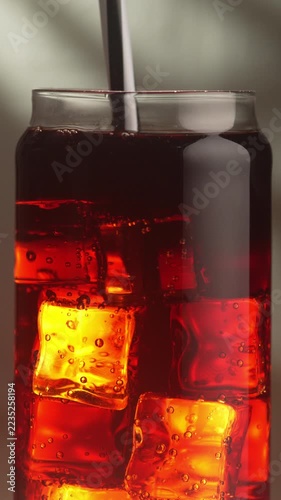 Close-up of a refreshing summer cocktail. A plastic drinking straw in a glass of a cold beverage stirs the ice cubes.