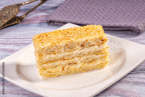 Fotografie Purple napkin and white plate on wooden surface, layered napoleon pastry dessert