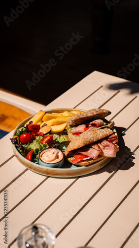 Fotografie Savory Sandwich Meal: A delicious sandwich served with crispy french fries, fresh salad, and a side of dipping sauce, all presented on a striped tablecloth, perfect for a casual lunch or light dinner