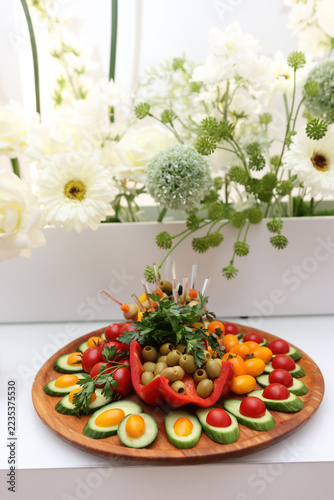 Vegetable appetizer with cucumbers, tomatoes, olives and herbs arranged on a wooden platter in a colorful decorative presentation.
