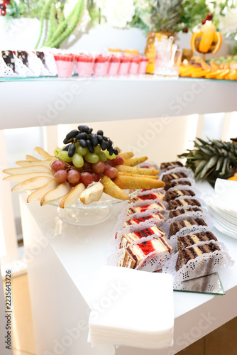 Festive buffet table with a fruit arrangement of grapes and pears, chocolate pastries and sliced sponge cake rolls.